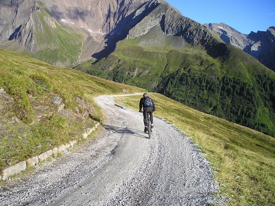 A picture of a cyclist biking on a trail towards a mountain field