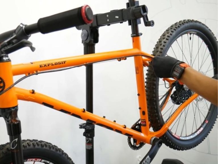 An orange bicycle being assembled - image focused on the bike frame