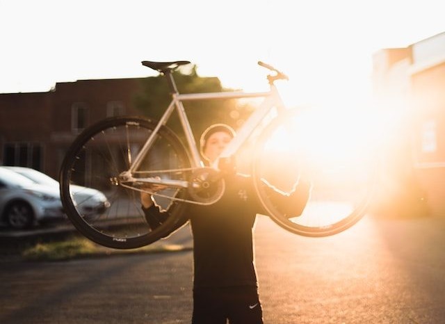 A guy in black outfit lifting a bike with sunlight covering upper portion of the image