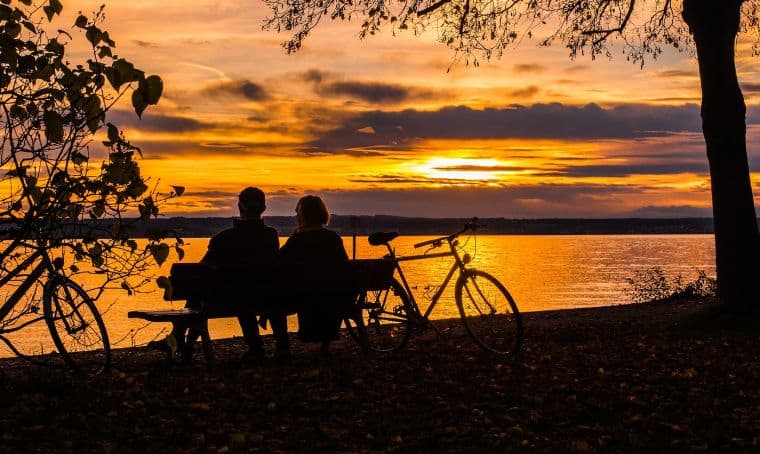 two persons looking at sunset with bike on the side