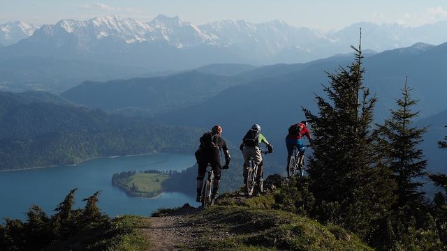 three mountain bikers on the edge of a cliff overlooking a lake